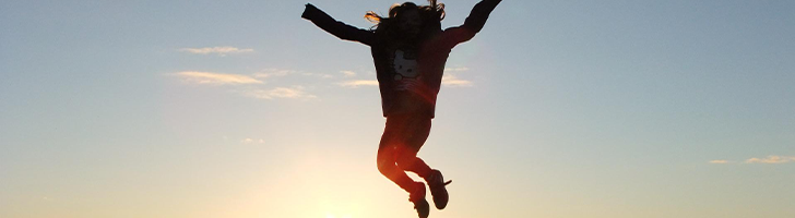 Woman jumping against background of rising sun