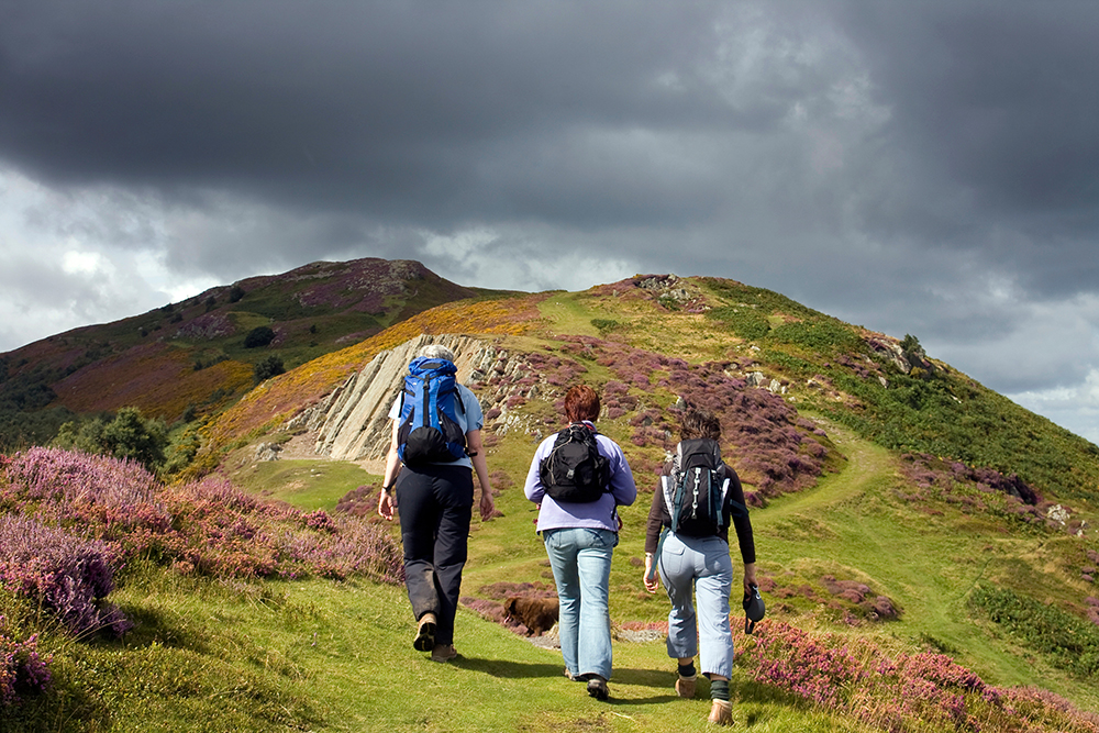 A photo of three hikers walking up a hill with backpacks in Conwy, Wales