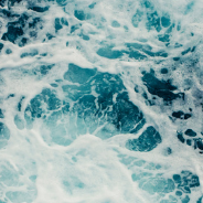 Deep blue seawater viewed from above, with lighter patches and white foam indicating choppy waters