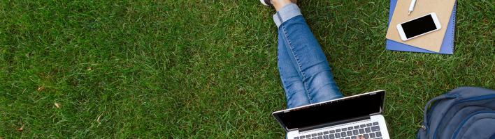 A birds eye view of a person with a laptop sitting on grass.