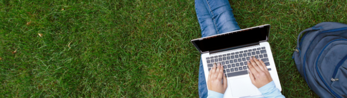 Student sitting on grass working on laptop