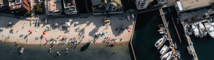 View from above of a beach with people on it, and to the right there are boats along a pier.