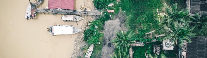 View from above of a coastal area with small boats and a pier nearby green tropical plants and houses.