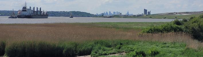 View of the Thames Estuary showing a boat in the top left corner and a view of London skyscapers in the distance in the top right corner.