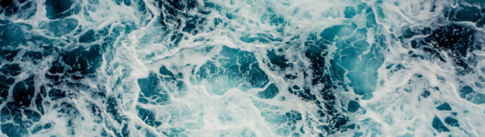 Deep blue seawater viewed from above, with lighter patches and white foam indicating choppy waters