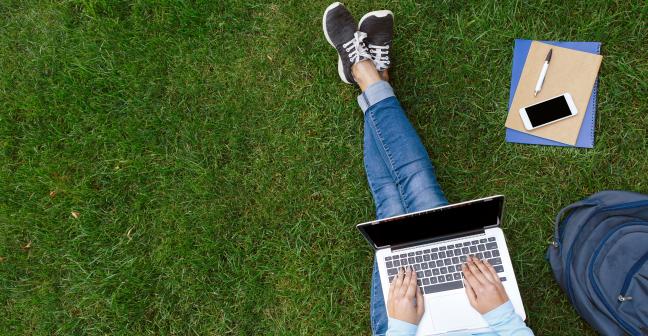 A birds eye view of a person with a laptop sitting on grass.