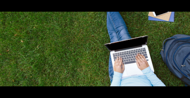 Student sitting on grass working on laptop