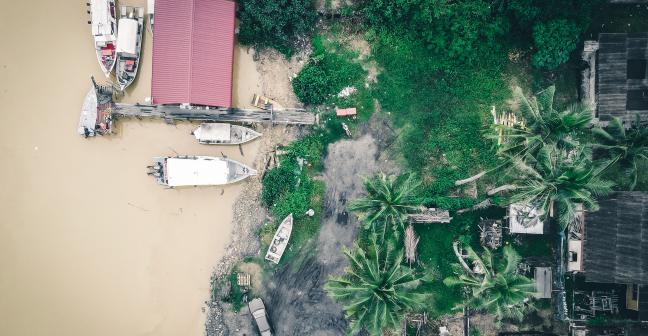 View from above of a coastal area with small boats and a pier nearby green tropical plants and houses.