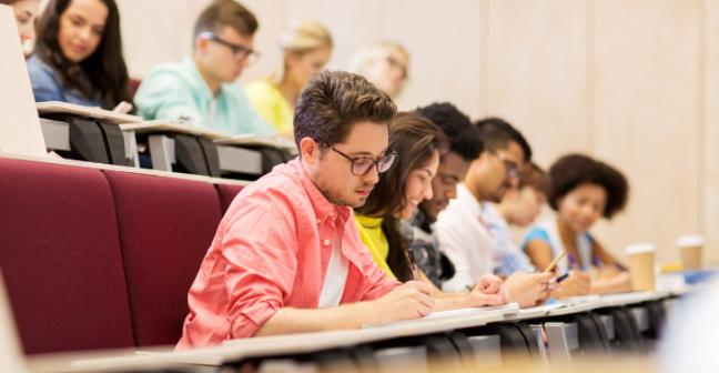 Students sat in a row in a lecture theatre taking notes