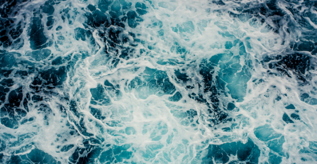 Deep blue seawater viewed from above, with lighter patches and white foam indicating choppy waters