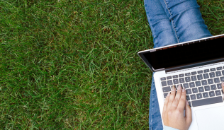 Student sitting on grass working on laptop