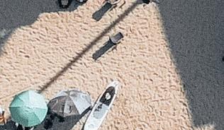 View from above of a beach with people on it, and to the right there are boats along a pier.