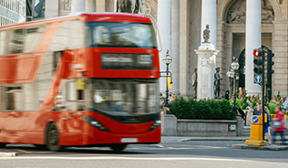 A red London bus drives past the London Exchange