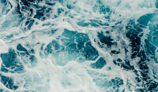 Deep blue seawater viewed from above, with lighter patches and white foam indicating choppy waters