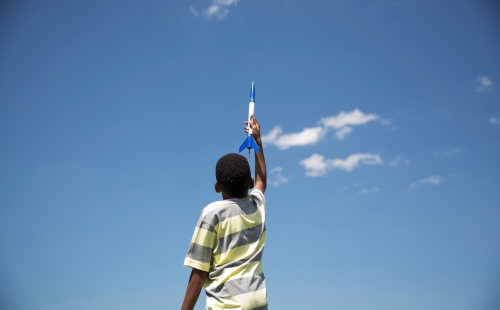A boy holding a toy rocket up to the sky.