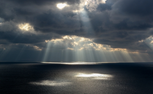 Sun breaking through grey clouds over the sea