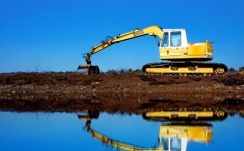 Yellow digger on soil reflected in water