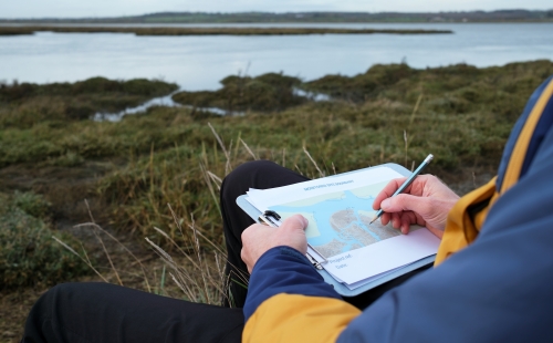 Scientist lying down, marking a paper map with a pencil in a coastal area 