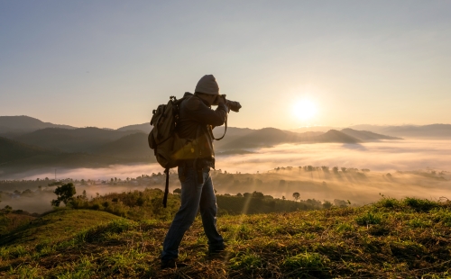 Man outside taking picture in field at sunrise 
