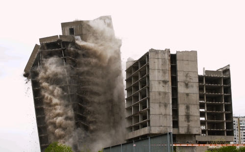 Grey blocks of flats being demolished by explosion