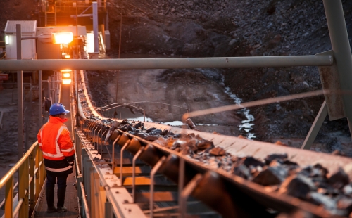 A worker inspects a conveyor belt of ore