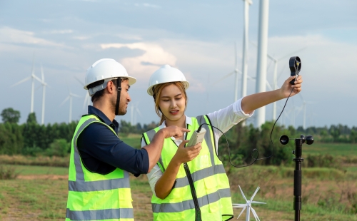 Young engineers using an anemometer to measure wind speed, temperature and humidity at a wind farm