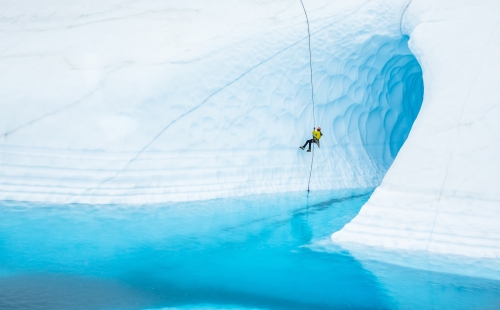 Person rappelling down a glacier with water below