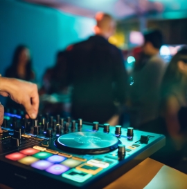 DJ plays live set and mixing music on turntable console at stage in the night club.