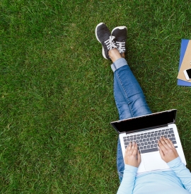 A birds eye view of a person working on a laptop sitting on grass