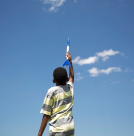 A boy holding a toy rocket up to the sky.
