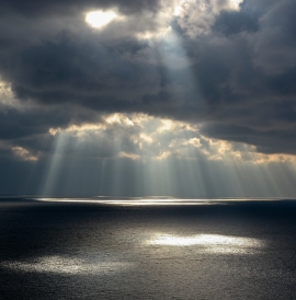 Sun breaking through grey clouds over the sea
