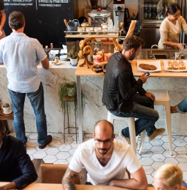 A busy cafe. People are seated enjoying coffee and pastries, and some are standing at the counter.